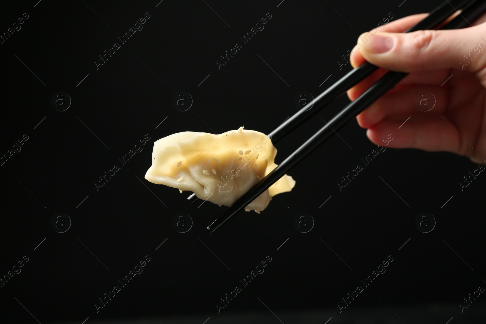 Photo of Woman holding chopsticks with tasty boiled gyoza (dumpling) on black background, closeup