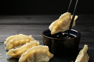 Photo of Dipping tasty gyoza (dumpling) into soy sauce at black wooden table, closeup