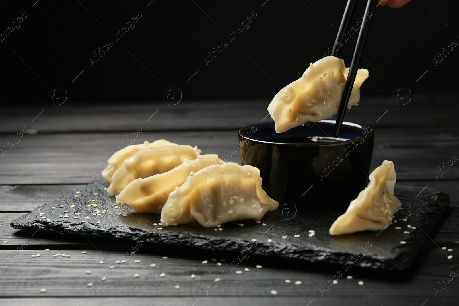 Photo of Dipping tasty gyoza (dumpling) into soy sauce at black wooden table, closeup