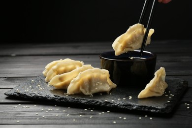 Photo of Dipping tasty gyoza (dumpling) into soy sauce at black wooden table, closeup