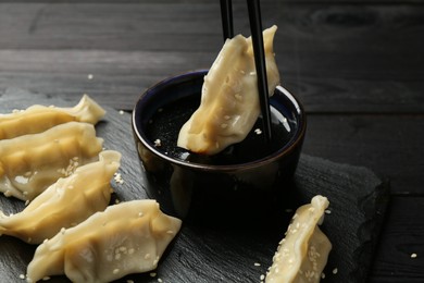 Photo of Dipping tasty gyoza (dumpling) into soy sauce at black wooden table, closeup