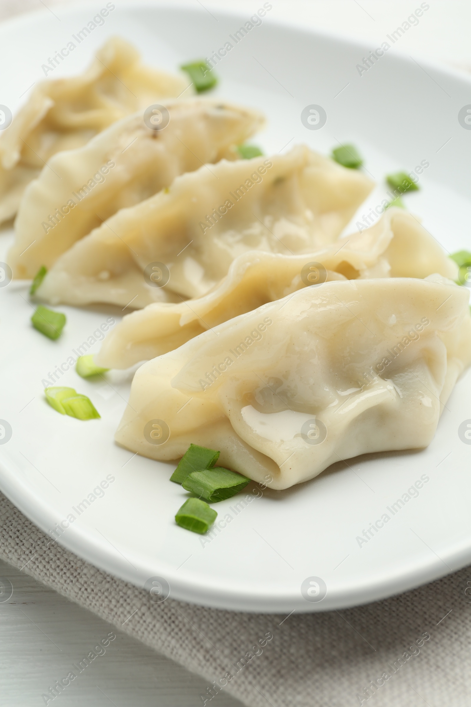 Photo of Tasty boiled gyoza (dumplings) with green onion on white table, closeup