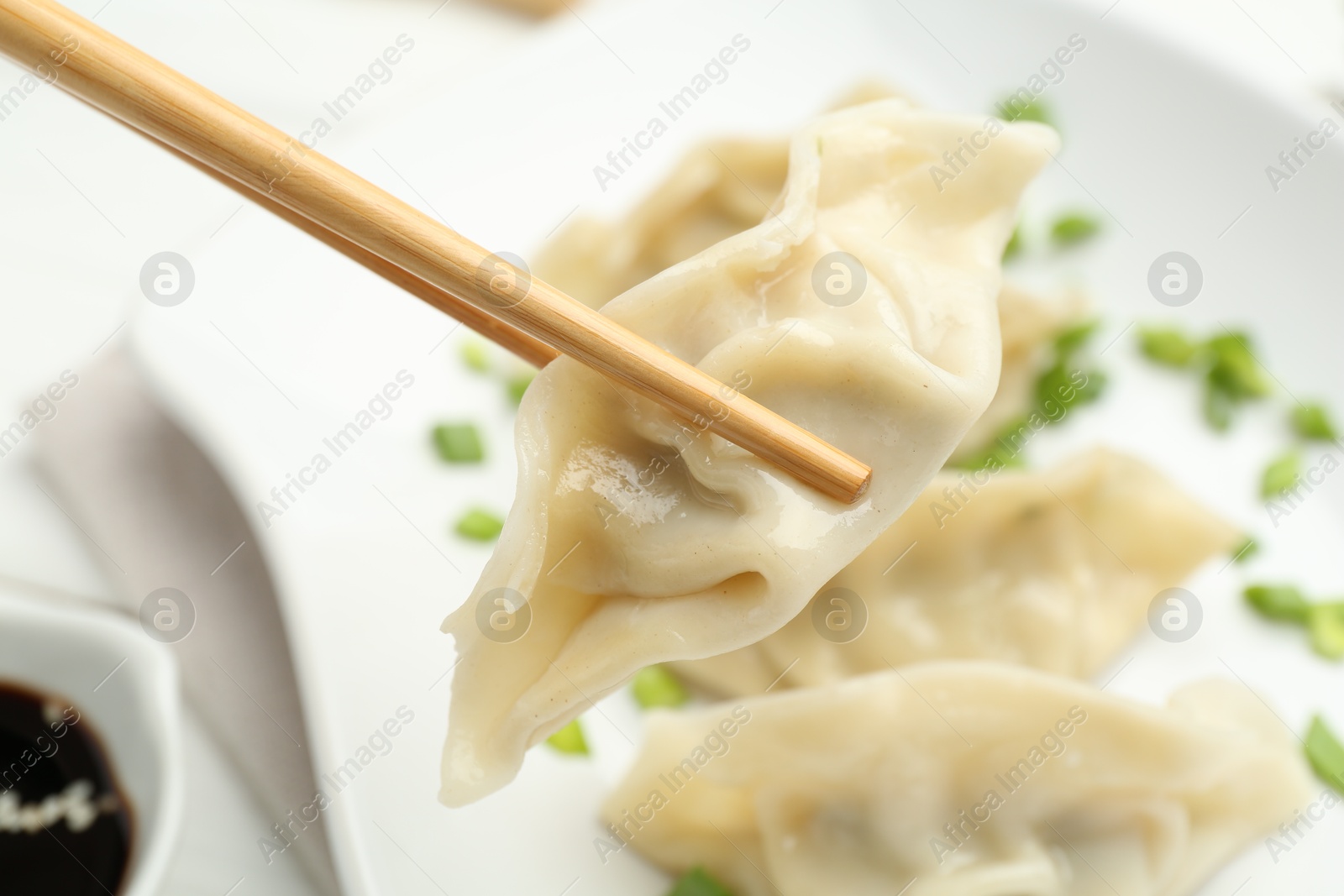 Photo of Chopsticks with tasty boiled gyoza (dumpling) over white table, closeup