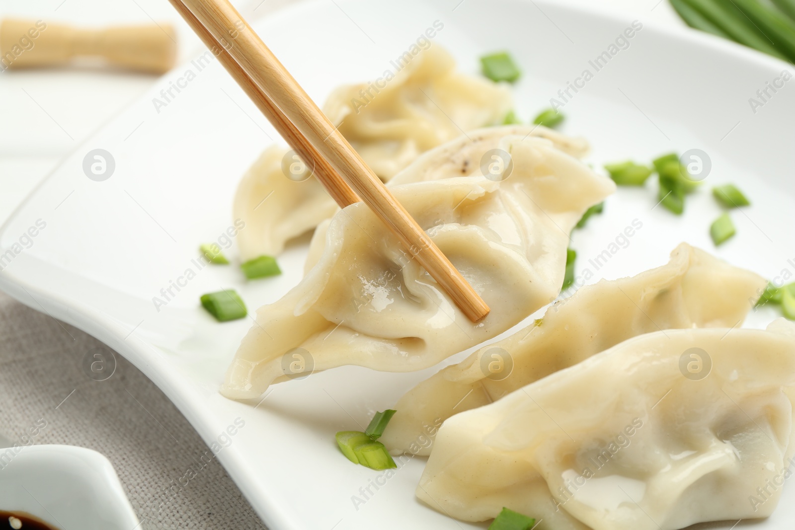 Photo of Taking tasty gyoza (dumpling) with chopsticks at table, closeup