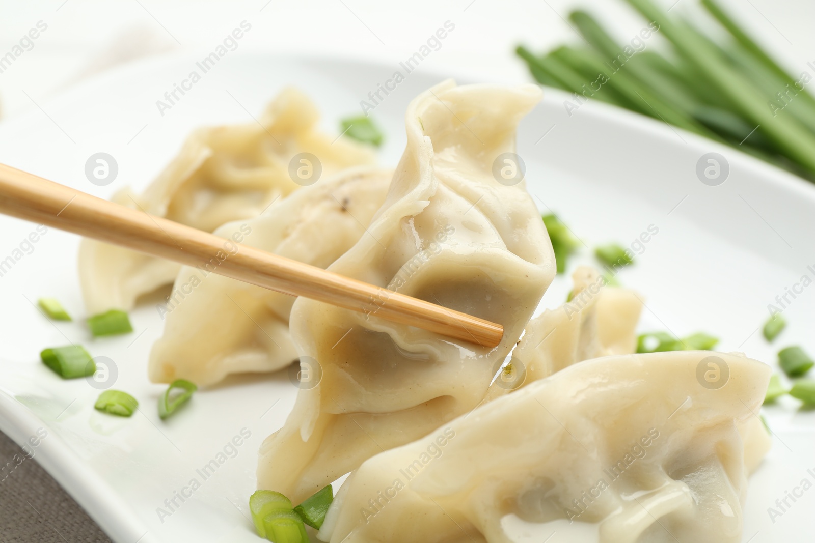 Photo of Taking tasty gyoza (dumpling) with chopsticks at table, closeup