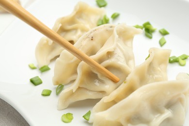 Photo of Taking tasty gyoza (dumpling) with chopsticks at table, closeup