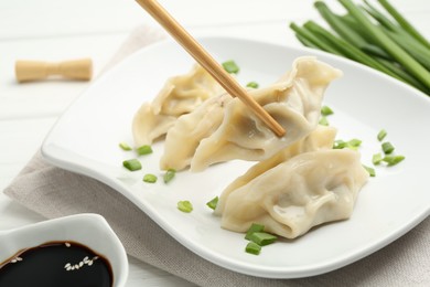 Photo of Taking tasty gyoza (dumpling) with chopsticks at white table