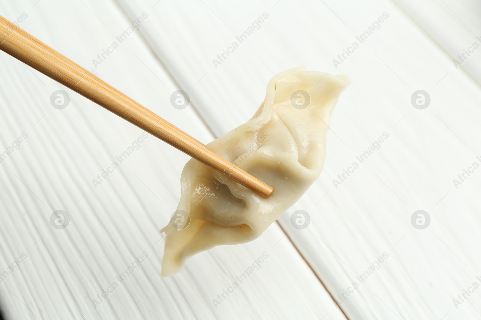 Photo of Chopsticks with tasty boiled gyoza dumpling over white wooden table, closeup