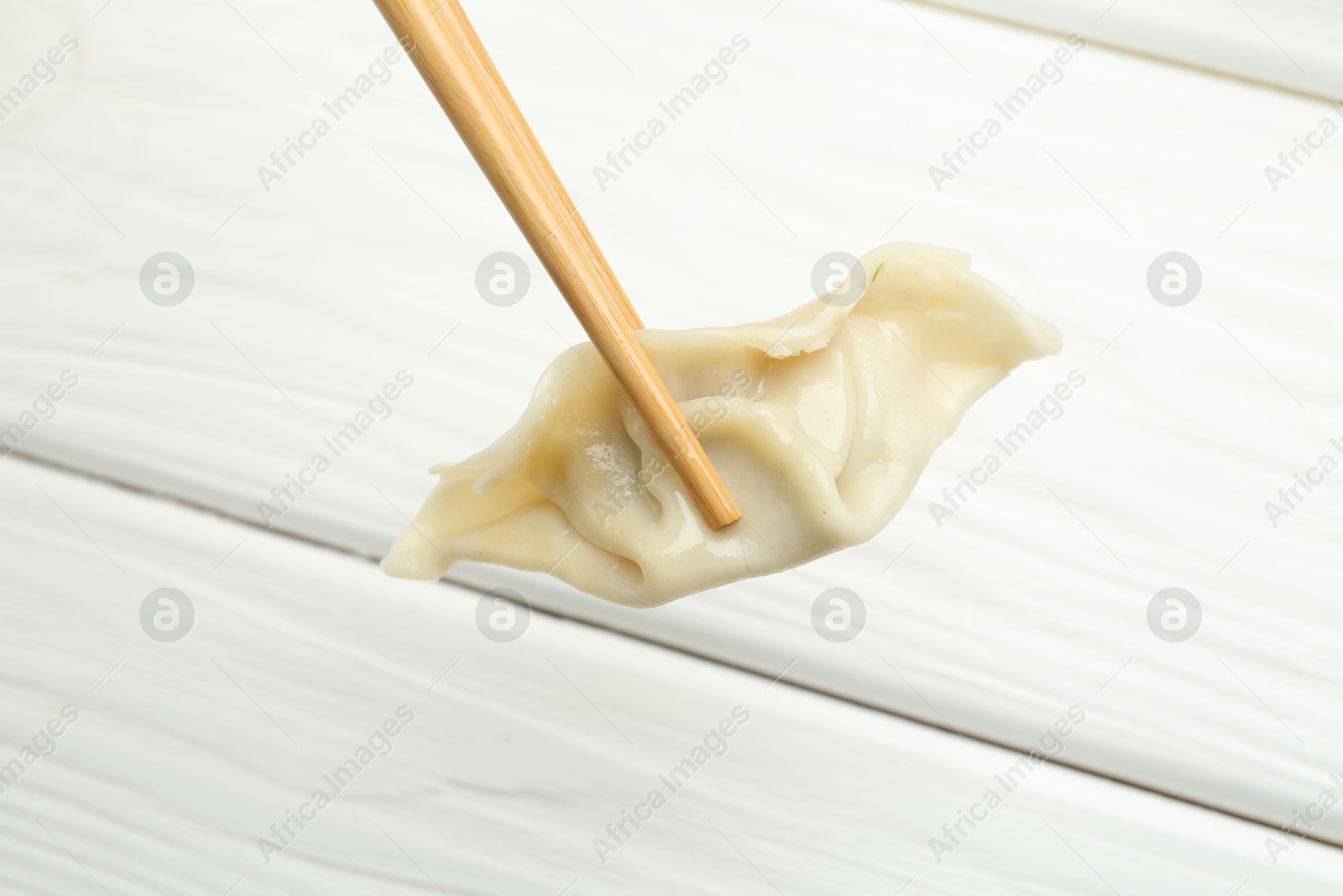 Photo of Chopsticks with tasty boiled gyoza dumpling over white wooden table, closeup