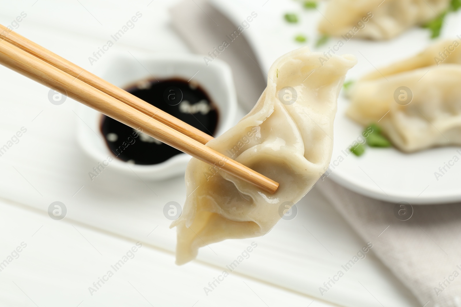 Photo of Chopsticks with tasty boiled gyoza (dumpling) over white table, closeup