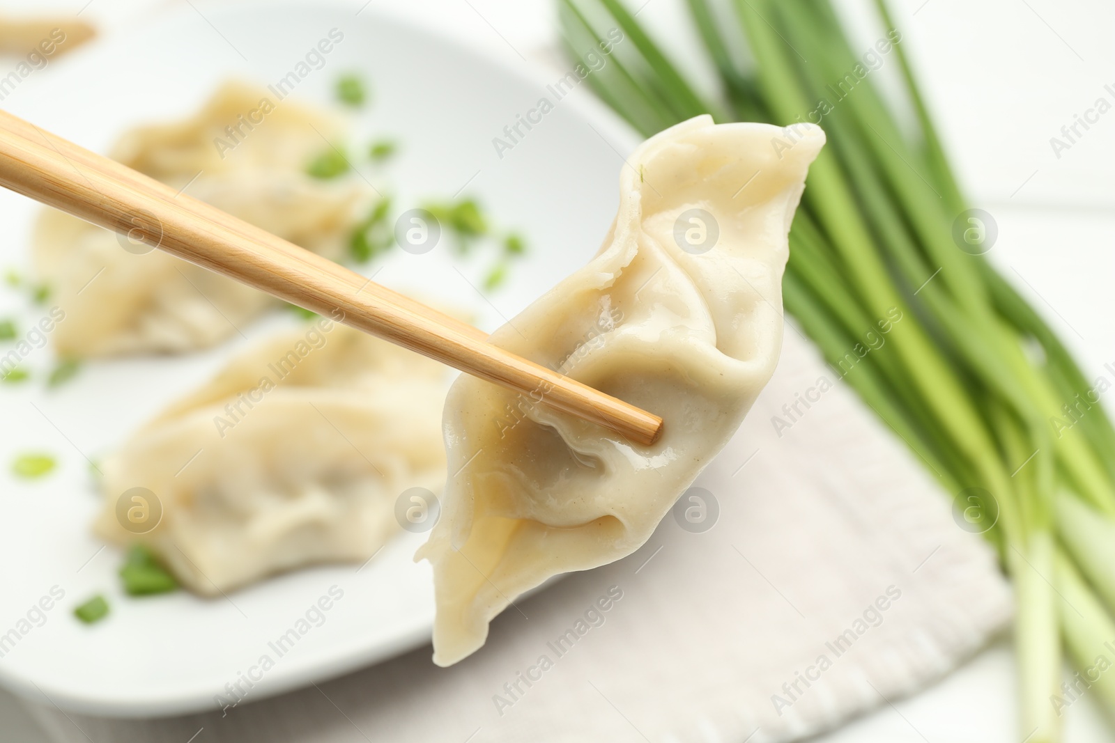 Photo of Chopsticks with tasty boiled gyoza (dumpling) over table, closeup