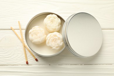 Photo of Beautiful flower-shaped candles in jar and matches on white wooden table, flat lay