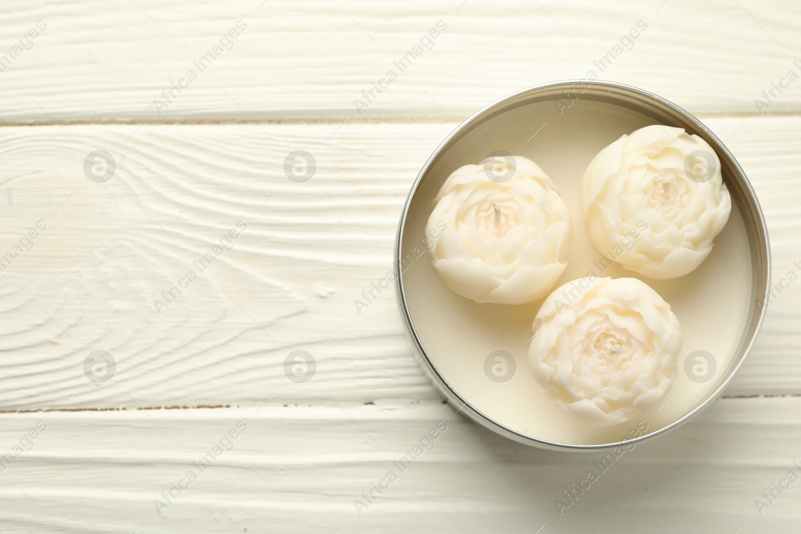 Photo of Beautiful flower-shaped candles in jar on white wooden table, top view. Space for text