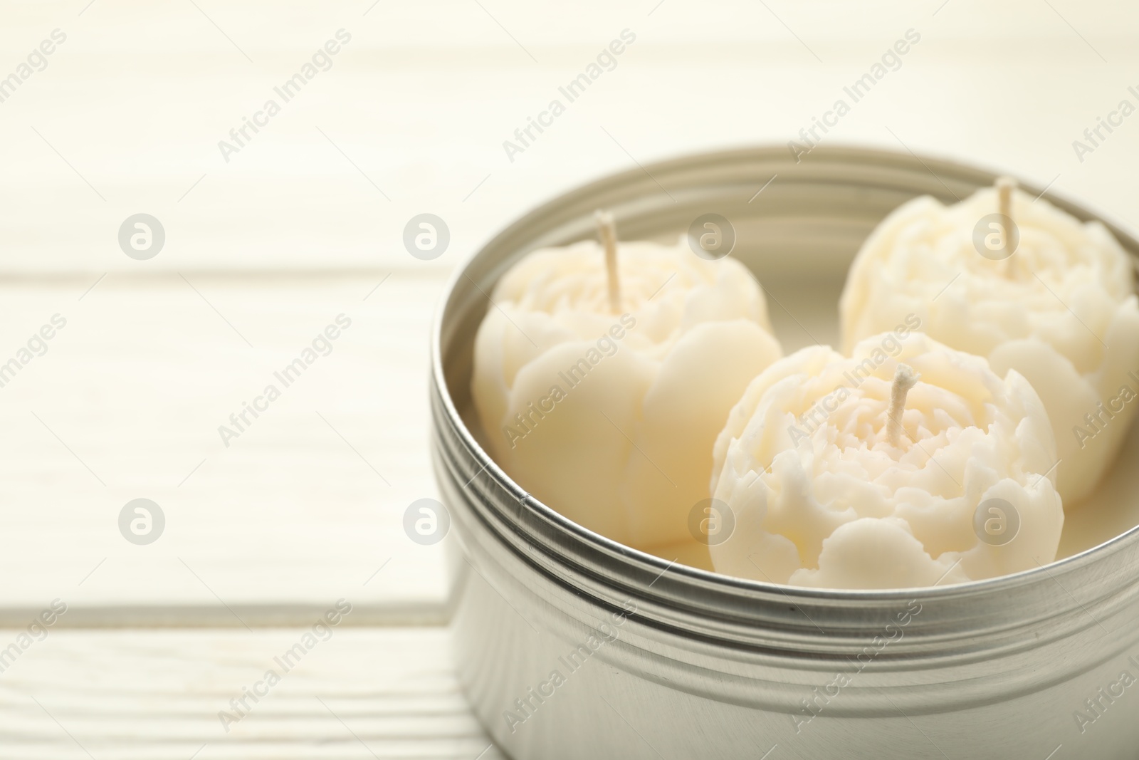 Photo of Beautiful flower-shaped candles in jar on white wooden table, closeup. Space for text