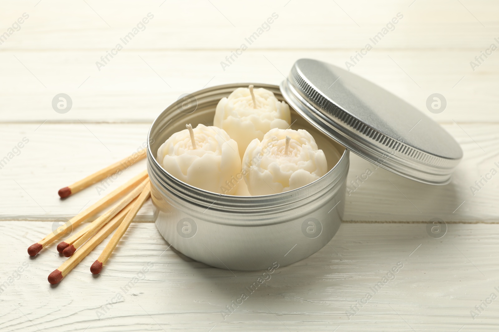 Photo of Beautiful flower-shaped candles in jar and matches on white wooden table, closeup