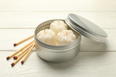 Photo of Beautiful flower-shaped candles in jar and matches on white wooden table, closeup