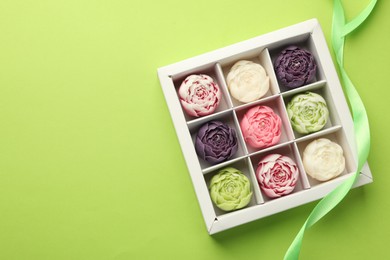 Photo of Beautiful flower-shaped candles in box and ribbon on light green background, top view. Space for text