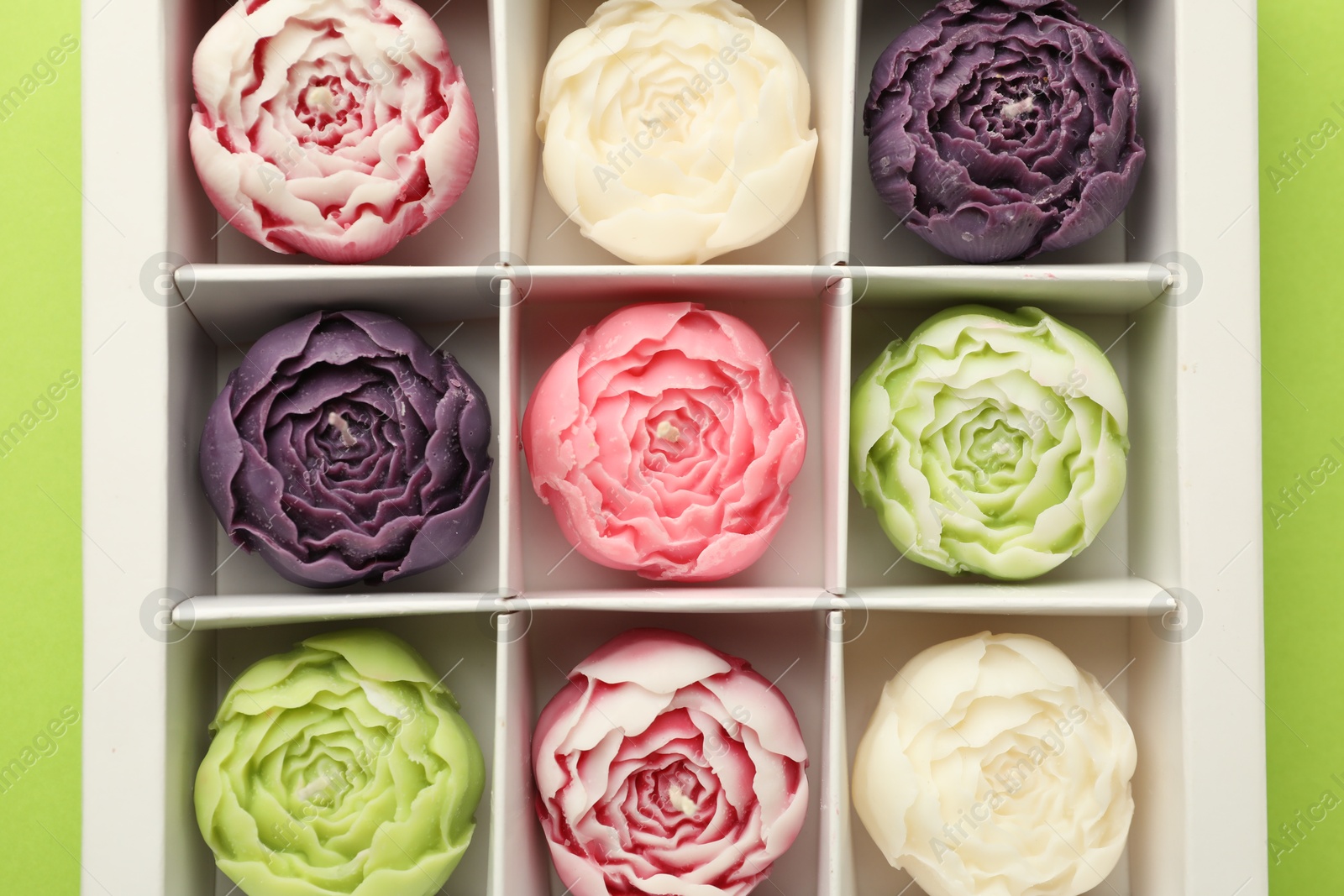 Photo of Beautiful flower-shaped candles in box on light green background, top view