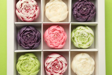 Photo of Beautiful flower-shaped candles in box on light green background, top view