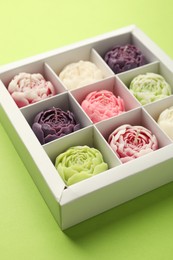 Photo of Beautiful flower-shaped candles in box on light green background, closeup