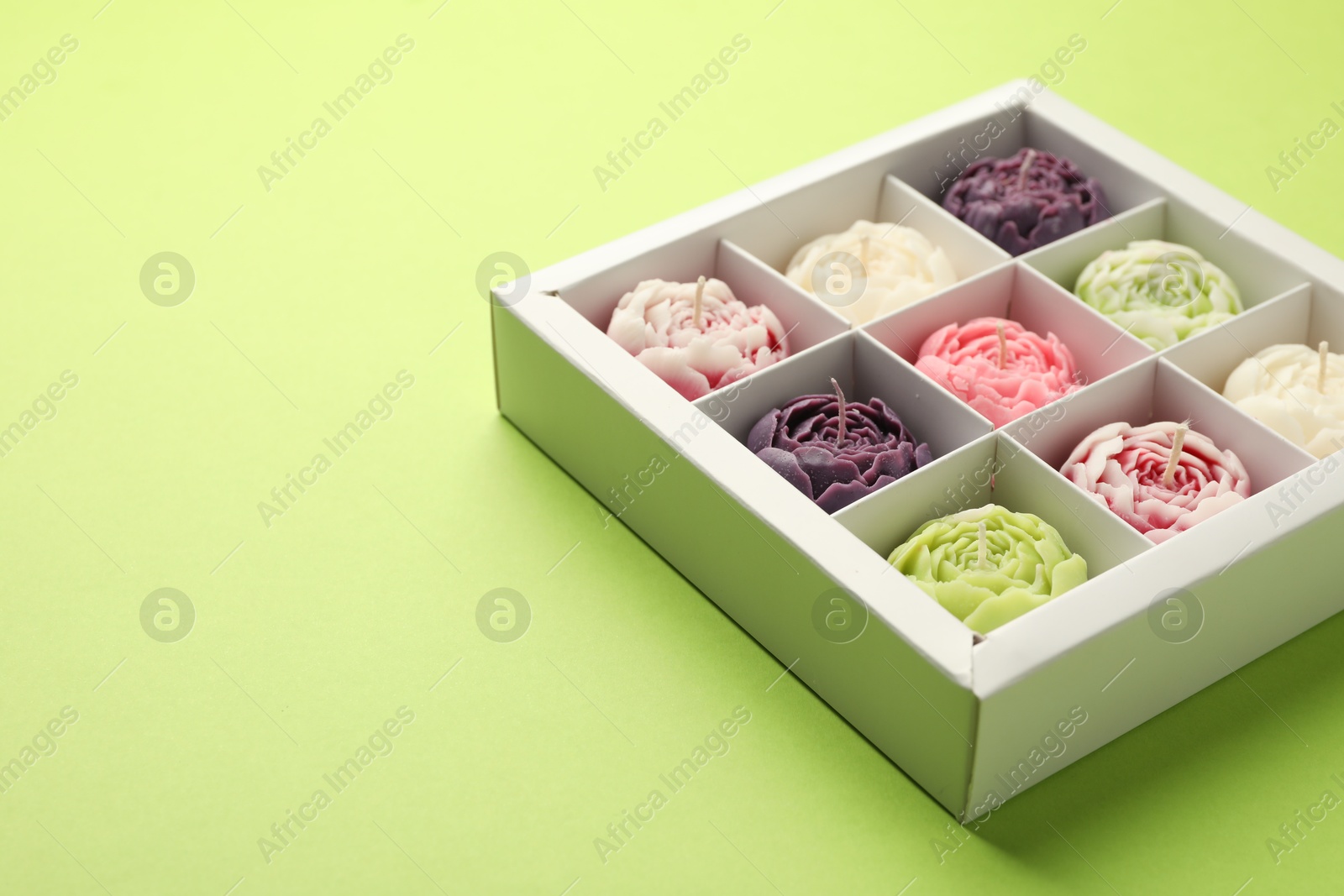 Photo of Beautiful flower-shaped candles in box on light green background, closeup. Space for text