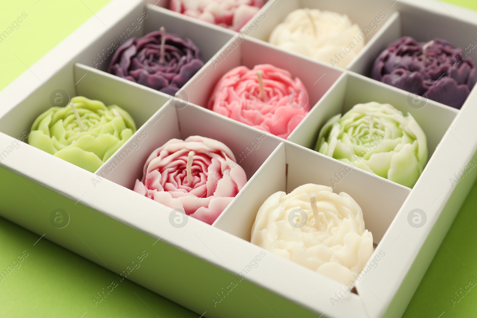 Photo of Beautiful flower-shaped candles in box on light green background, closeup