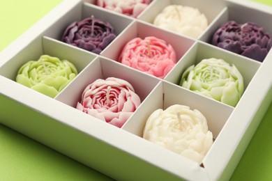 Photo of Beautiful flower-shaped candles in box on light green background, closeup