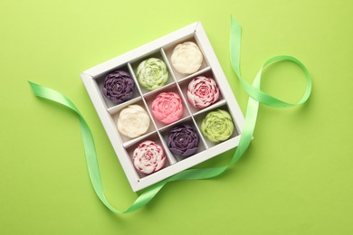 Photo of Beautiful flower-shaped candles in box and ribbon on light green background, top view