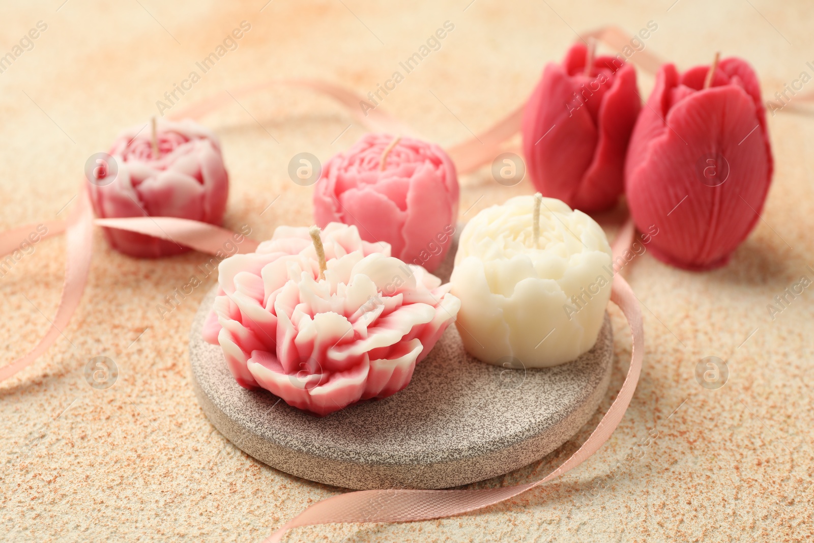 Photo of Beautiful flower-shaped candles and ribbon on beige textured background, closeup