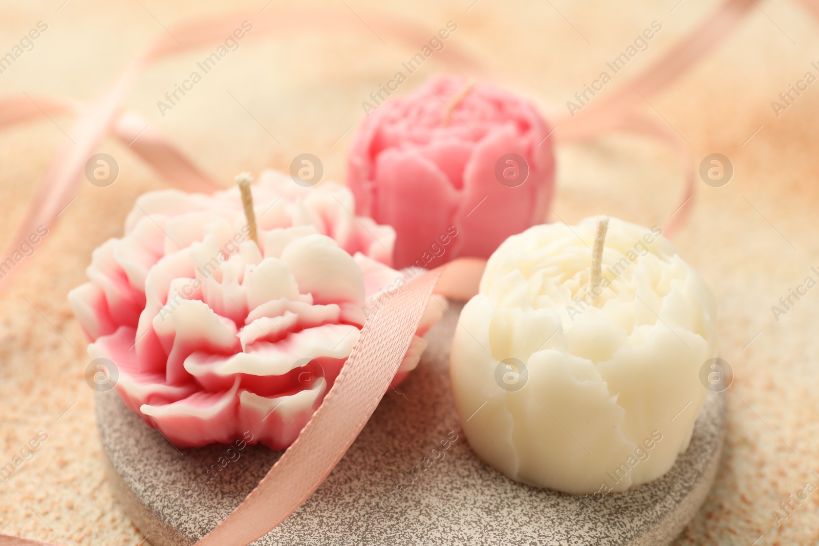 Photo of Beautiful flower-shaped candles and ribbon on beige background, closeup