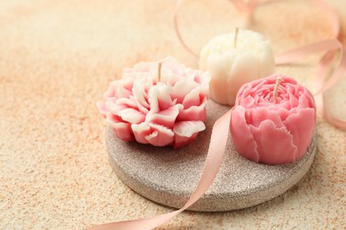 Photo of Beautiful flower-shaped candles and ribbon on beige textured background, closeup