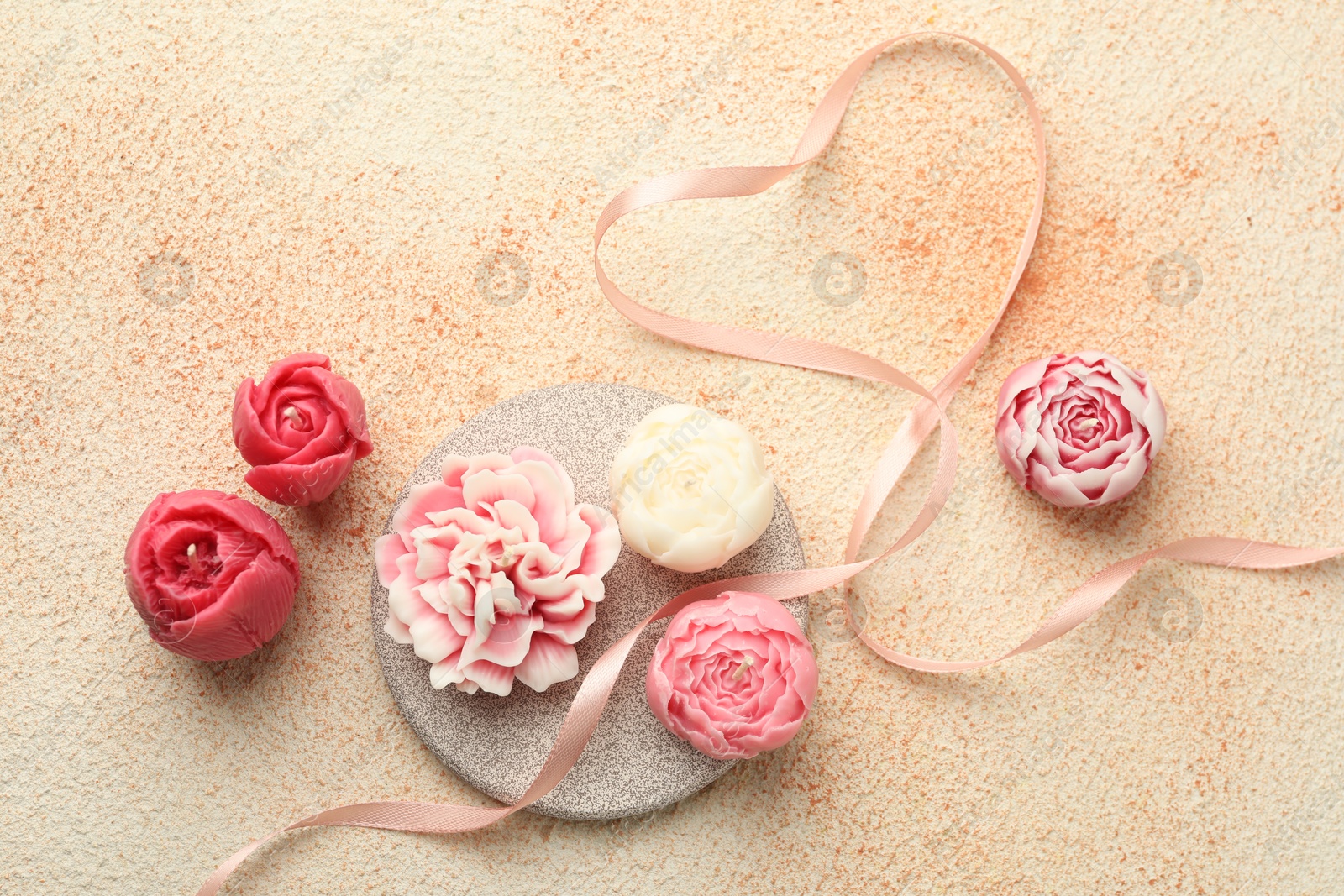 Photo of Beautiful flower-shaped candles and ribbon on beige textured background, flat lay