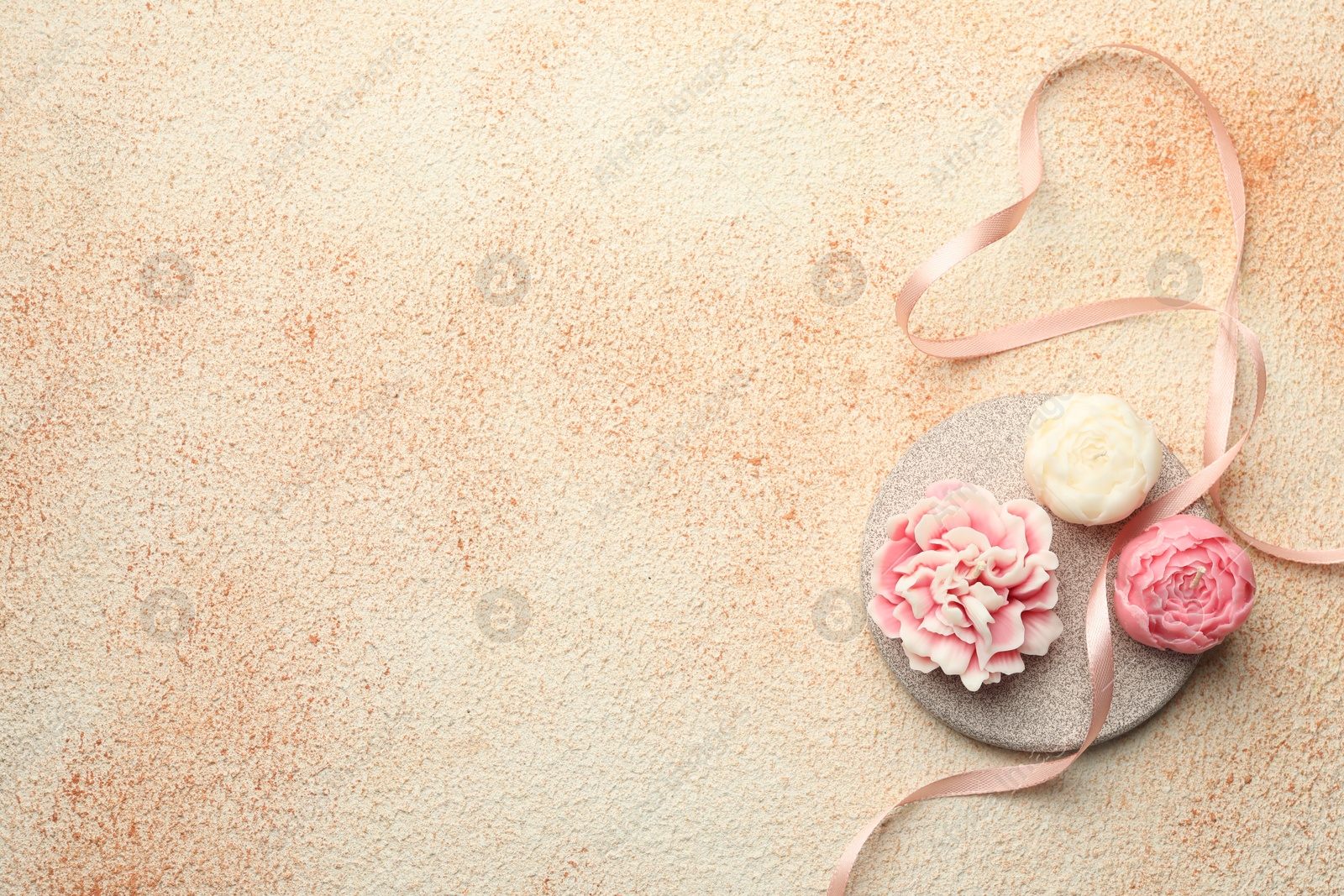 Photo of Beautiful flower-shaped candles and ribbon on beige textured background, top view. Space for text