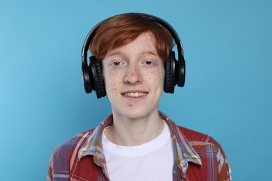 Photo of Smiling teenage boy with freckles listening to music by headphones on light blue background