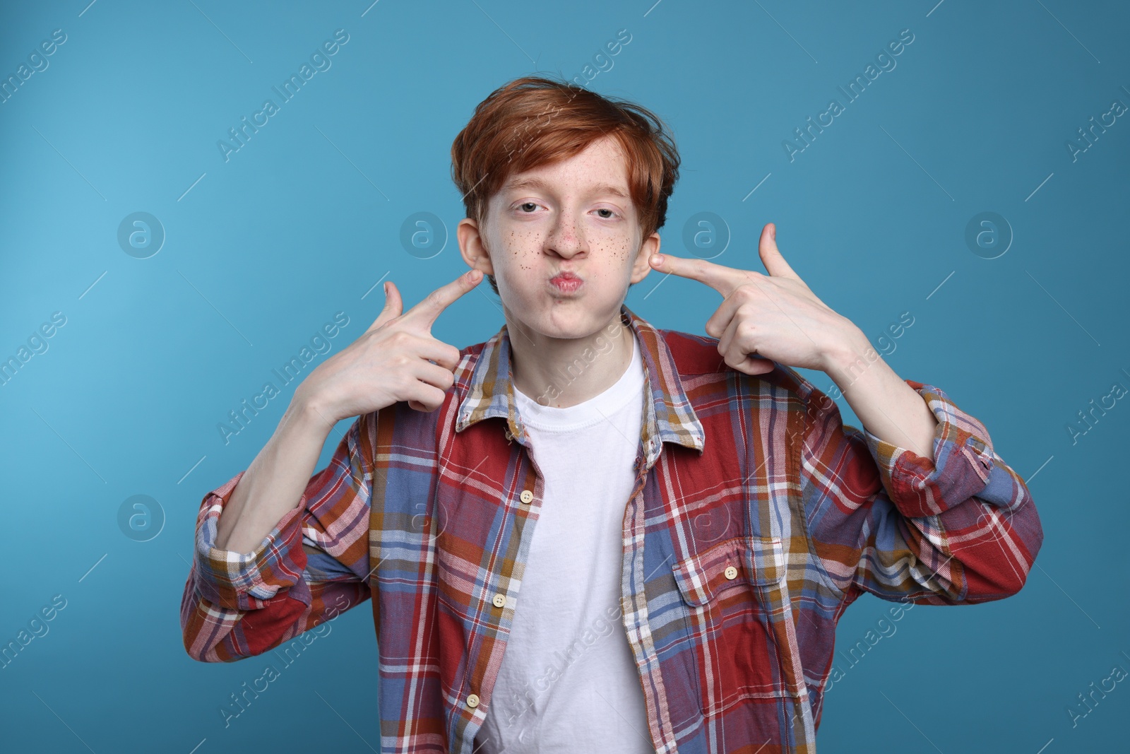 Photo of Funny teenage boy with freckles on light blue background