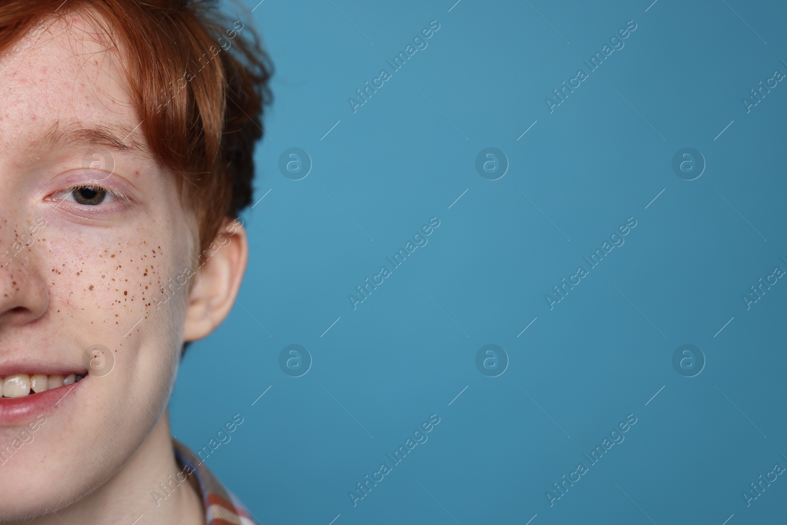 Photo of Smiling teenage boy with freckles on light blue background, closeup. Space for text