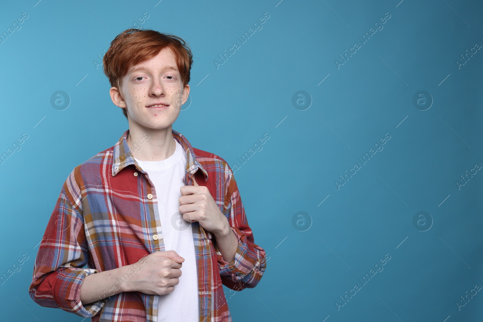 Photo of Smiling teenage boy with freckles on light blue background. Space for text