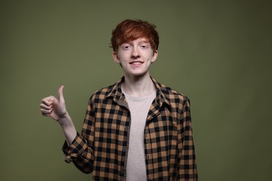 Photo of Smiling teenage boy with freckles showing thumbs up on dark green background