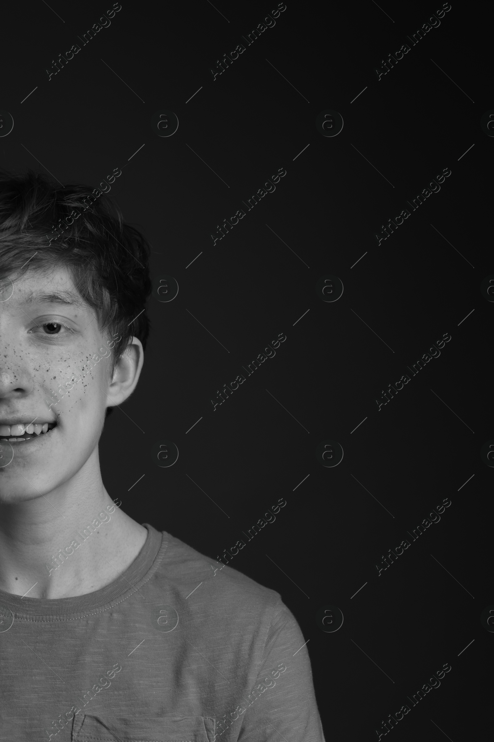 Photo of Smiling teenage boy with freckles on dark background, black and white effect. Space for text