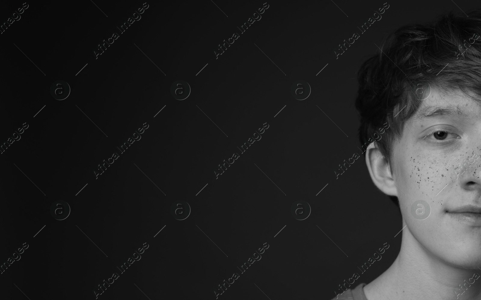 Photo of Teenage boy with freckles on dark background, black and white effect. Space for text