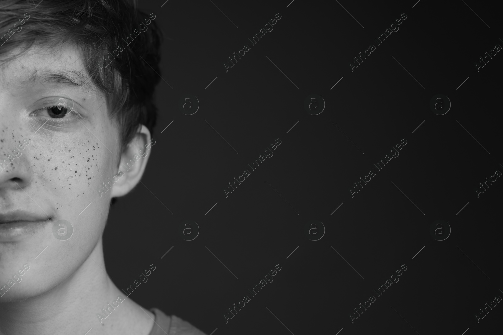 Photo of Teenage boy with freckles on dark background, black and white effect. Space for text