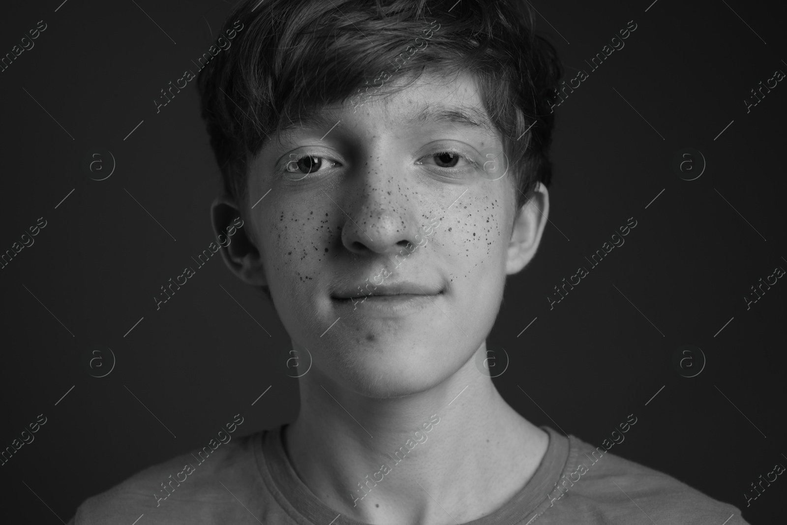 Photo of Teenage boy with freckles on dark background, black and white effect