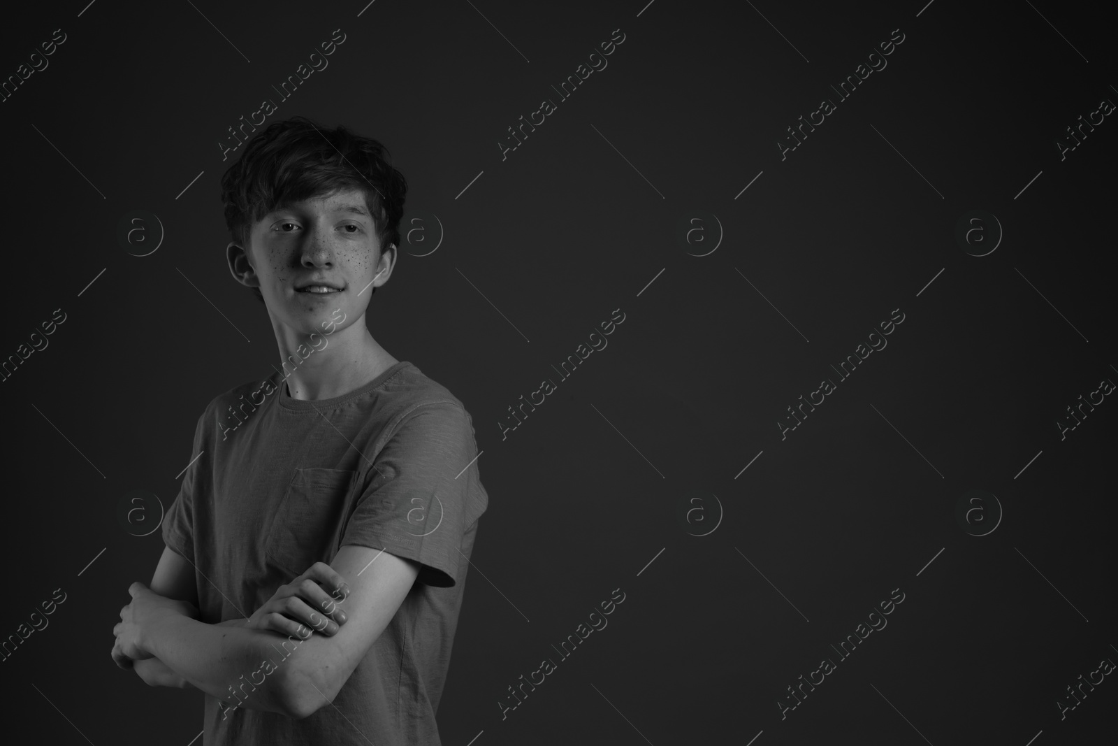 Photo of Smiling teenage boy with freckles on dark background, black and white effect. Space for text