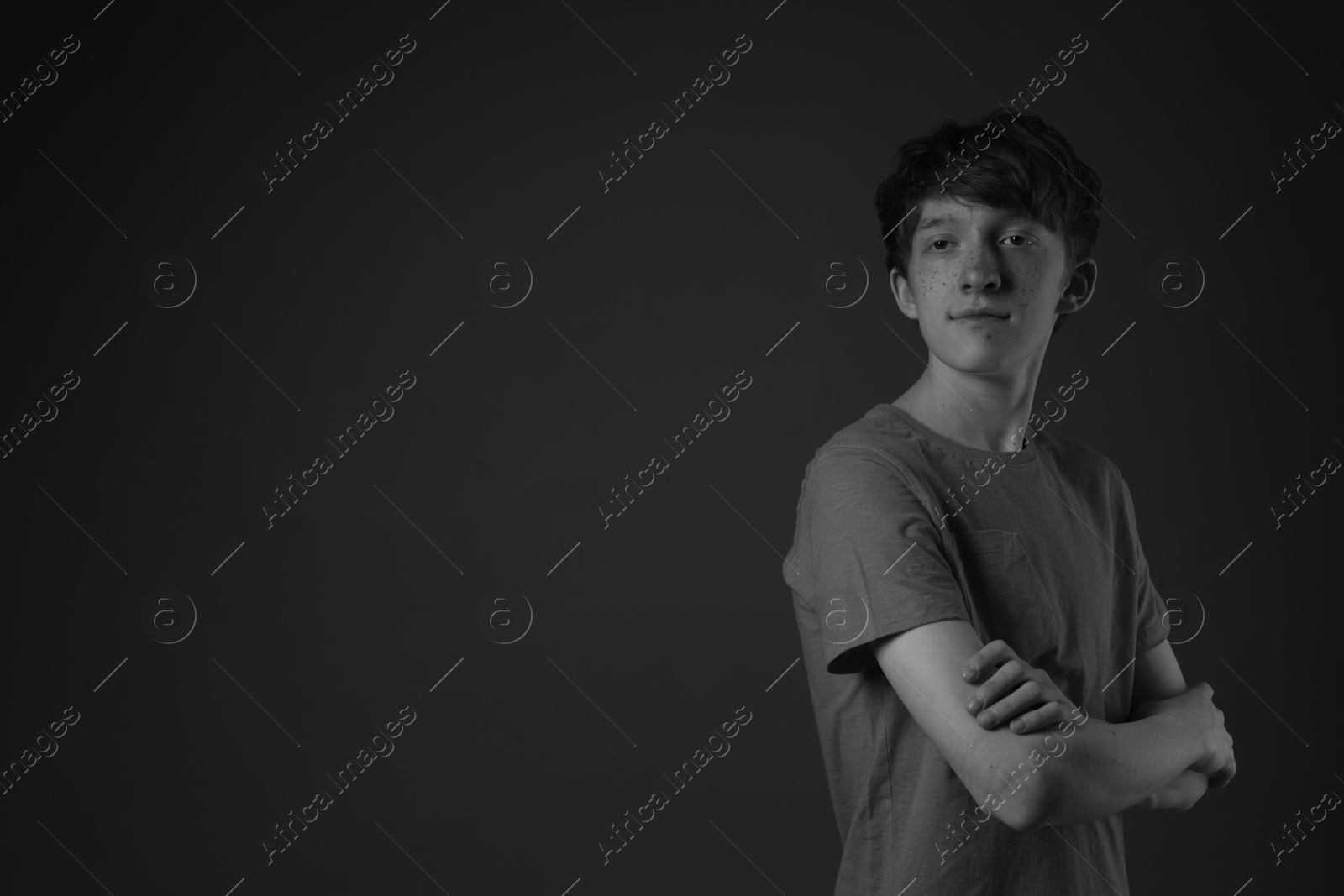 Photo of Teenage boy with freckles on dark background, black and white effect. Space for text