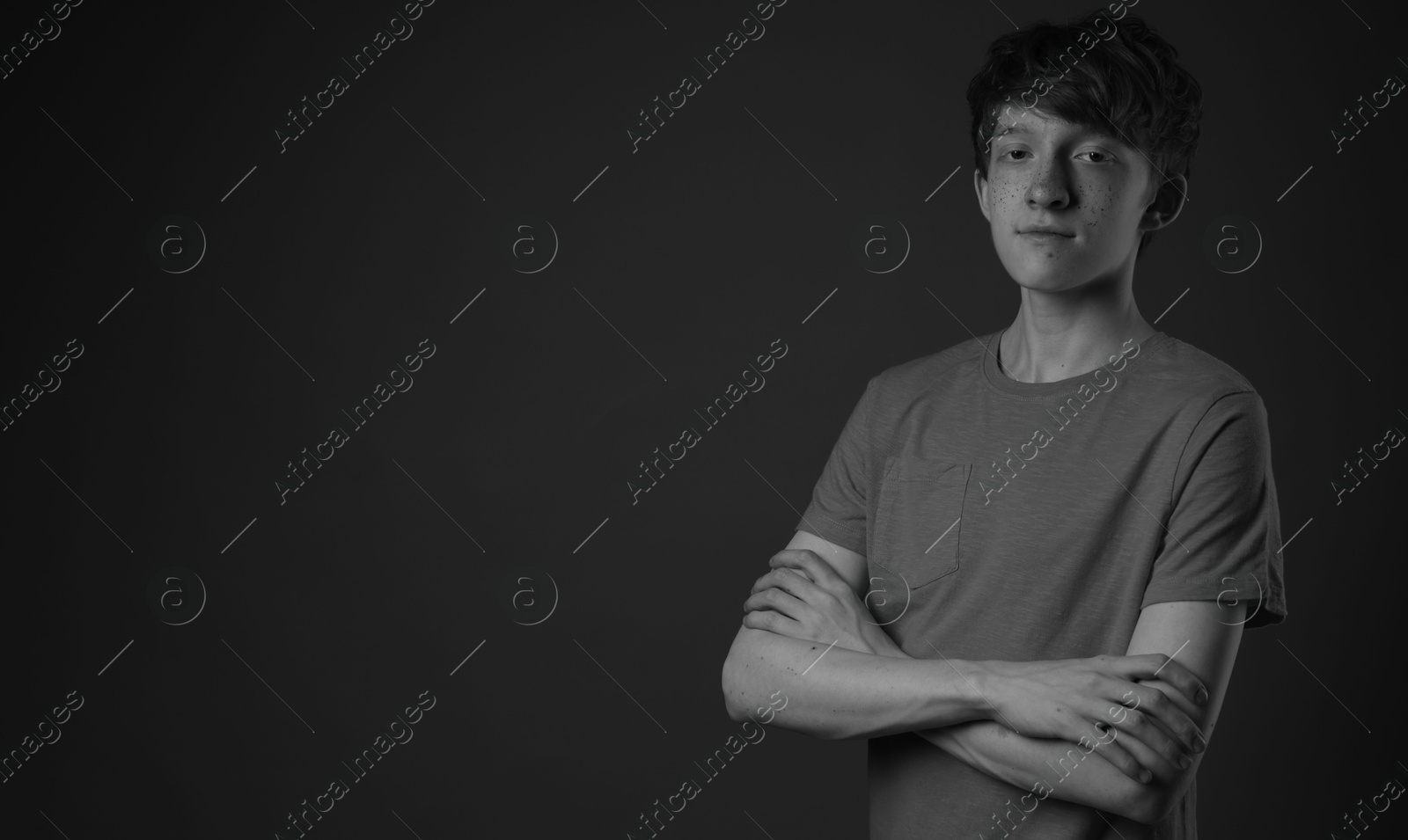 Photo of Teenage boy with freckles on dark background, black and white effect. Space for text