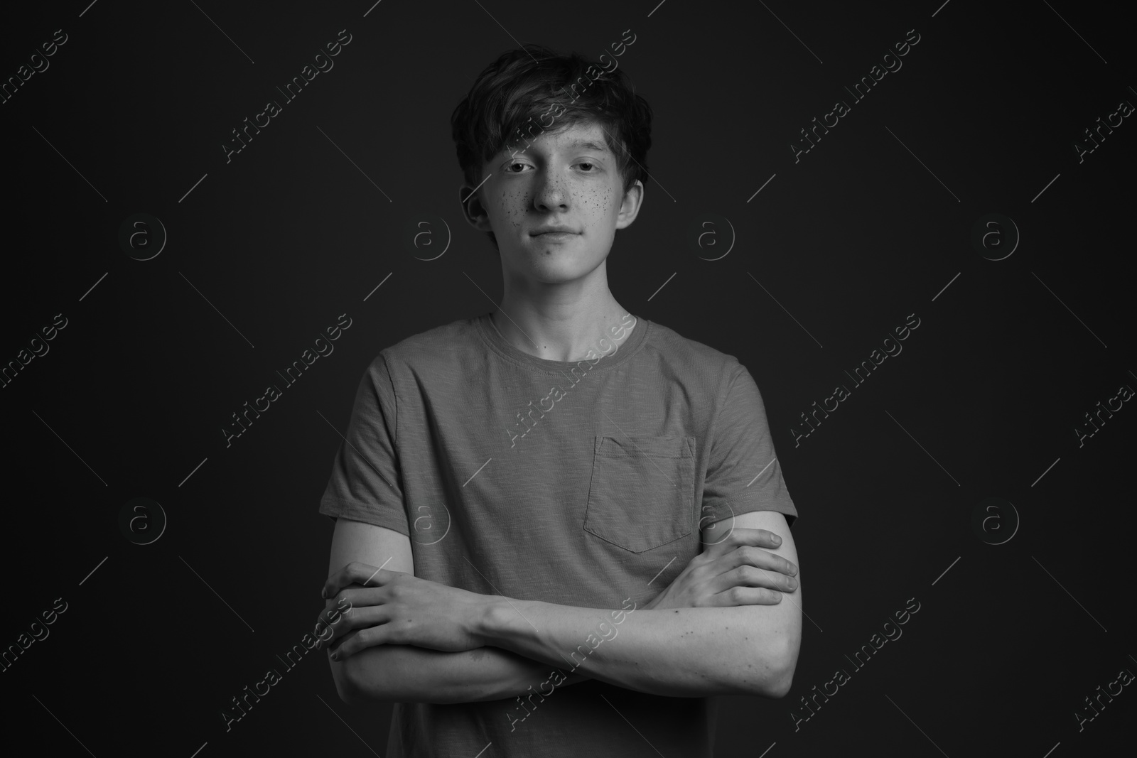 Photo of Portrait of teenage boy with freckles on dark background, black and white effect