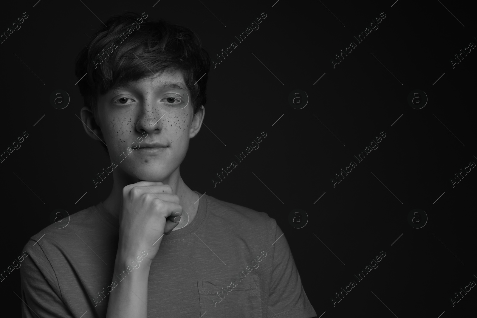 Photo of Teenage boy with freckles on dark background, black and white effect. Space for text