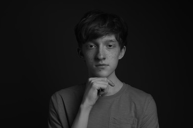 Photo of Portrait of teenage boy with freckles on dark background, black and white effect