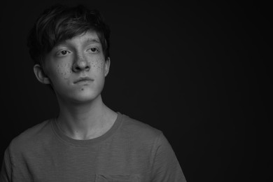 Photo of Teenage boy with freckles on dark background, black and white effect. Space for text