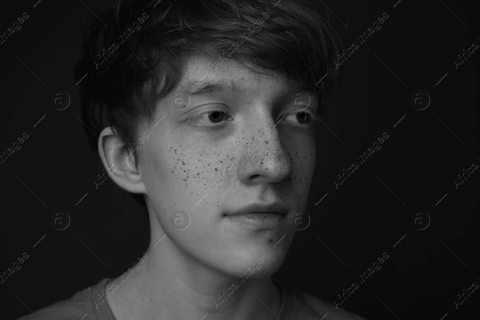 Photo of Teenage boy with freckles on dark background, closeup. Black and white effect